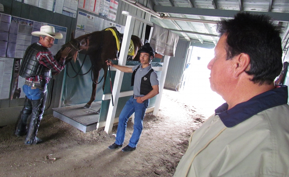 Leandro Mora (right) watches two hot walkers as they administer vibration plate therapy on three-year-old horse Watchkeeper at the Santa Anita Race Track June 6. Photo by Aaron Castrejon.